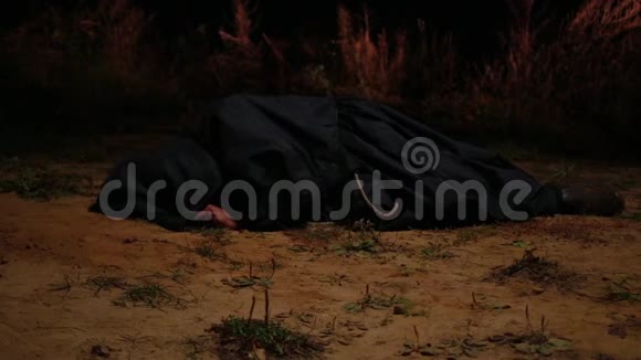 一个穿着黑色长袍的和尚躺在地上的黑暗中一团火在他周围点燃安全视频的预览图