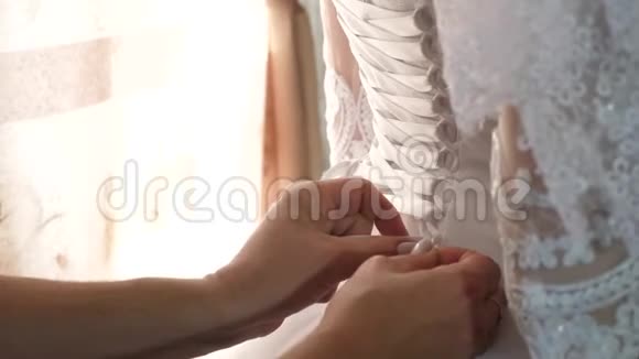 新娘穿一件白色婚纱新娘的女仆把丝带系在新娘衣服的背面女孩穿的是视频的预览图