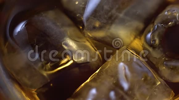 一大片冰块漂浮在桌子上一杯陈年的金色威士忌中用r合上琥珀色酒精饮料视频的预览图