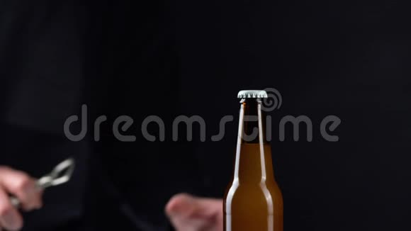 男人打开黑色背景上带帽子的冷啤酒瓶双手打开冷藏小麦或啤酒视频的预览图