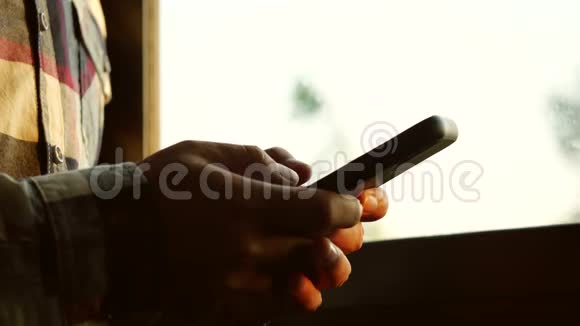 男人在有窗户背景的房间里使用智能手机早上使用智能手机进行社交媒体或聊天视频的预览图