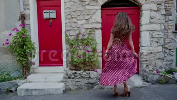 穿着红色波尔卡多礼服的浪漫女孩在红色的中世纪旧门附近旋转微笑着在古城旅行视频的预览图