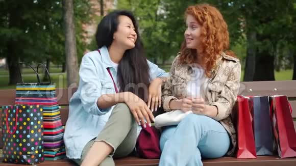 快乐的青少年在公园的长凳上慢腾腾地拿着购物袋聊天视频的预览图