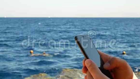 男性在海水背景下使用黑色智能手机视频的预览图