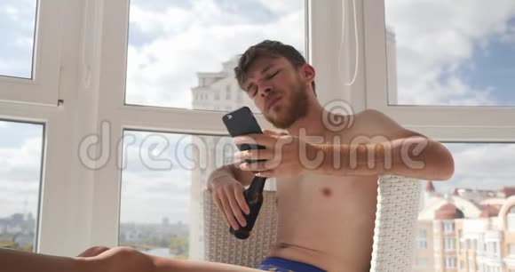 醉酒的年轻人穿着内裤坐在家里在手机上输入信息喝酒视频的预览图