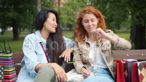 在公园里坐在长凳上聊天的漂亮女孩在购物袋里买东西视频的预览图