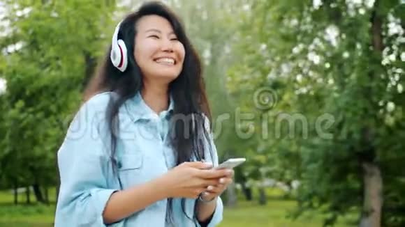 亚洲学生使用智能手机在户外戴耳机跳舞的慢动作视频的预览图