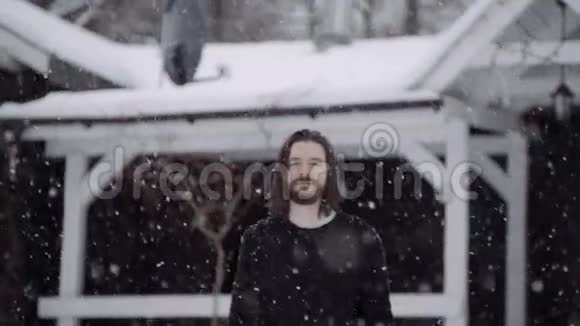 穿着黑色毛衣的英俊男子站在一座古老的木屋前落着雪视频的预览图