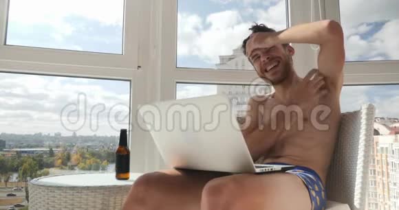 年轻的醉汉白种人无胡子的男人穿着内裤坐在阳台上狂笑视频的预览图