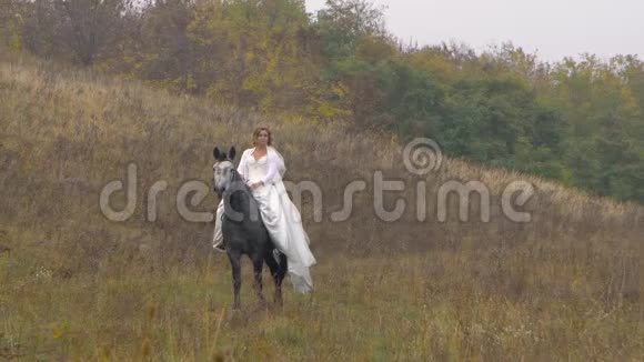 美丽的未婚妻穿着白色连衣裙骑着一匹靠近木头的马视频的预览图
