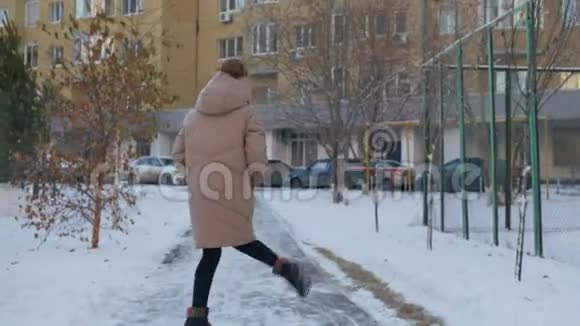 快乐的女人穿着米色羽绒服和柚子帽在雪城的冬天散步在雪地里跳舞的快乐女孩视频的预览图