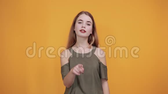 可爱的年轻女子穿着秋葵橙色衬衫手指在脸颊上微笑着视频的预览图