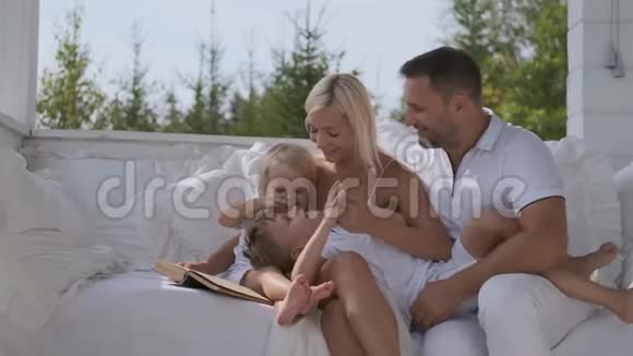 年轻幸福的家庭爸爸妈妈和两个儿子坐在房子附近明亮的阳台上玩得很开心视频的预览图