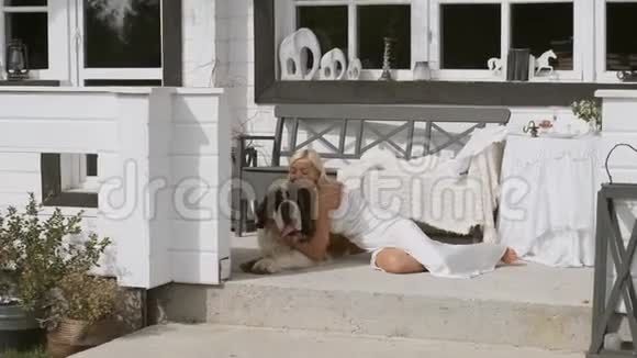 一个年轻的女孩抱着一只大狗坐在房子附近的门廊上微笑总体计划视频的预览图