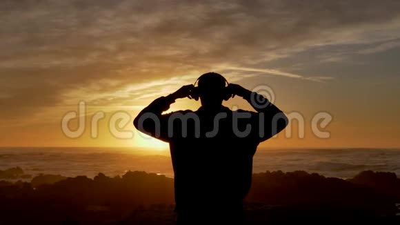 穿着无线耳机慢动作走路的男人看着美丽的的波浪在加州召唤着美丽的日落视频的预览图