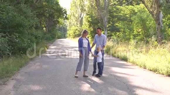 一个幸福的家庭有一个年轻的儿子在树林里的一条空路上散步旅行视频的预览图