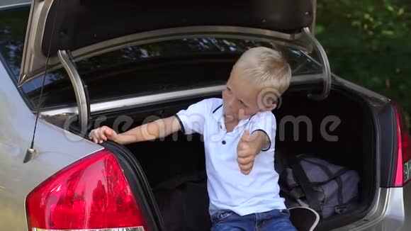 活泼开朗的小男孩坐在汽车的后备箱里竖起大拇指视频的预览图