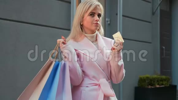 拿着纸袋和信用卡的女士站在商店附近的街道上视频的预览图
