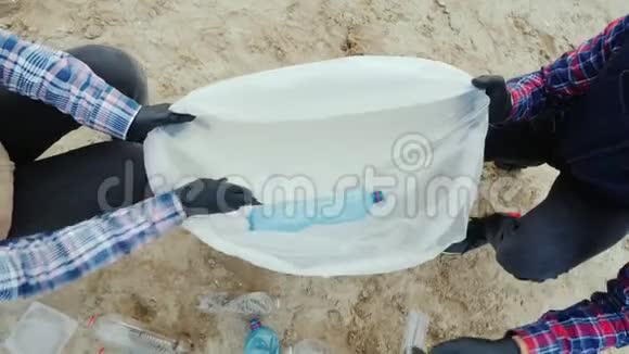 志愿者把塑料垃圾放进袋子里清洁海滩爱护环境顶部视图视频的预览图