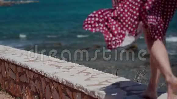 穿着红色夏装的女孩赤着脚在海边的石栏上奔跑后景女性腿部特写视频的预览图