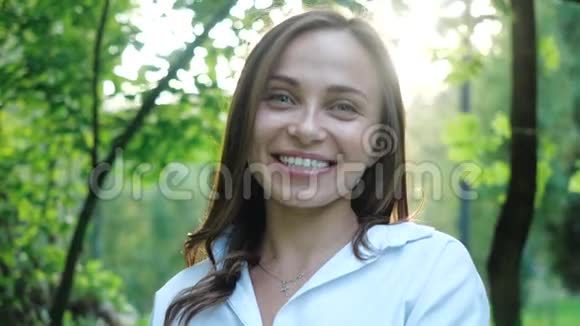 一位美丽的微笑女人身穿白色衬衫的婚纱摄影师正在公园里用专业相机拍摄照片视频的预览图