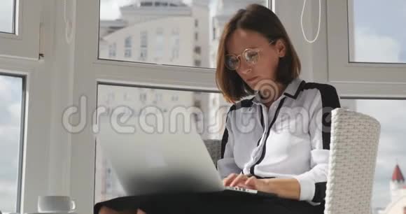 愤怒的女商人穿着严格的衣服戴着眼镜在现代办公室的笔记本电脑上工作快速地打字看着显示器视频的预览图