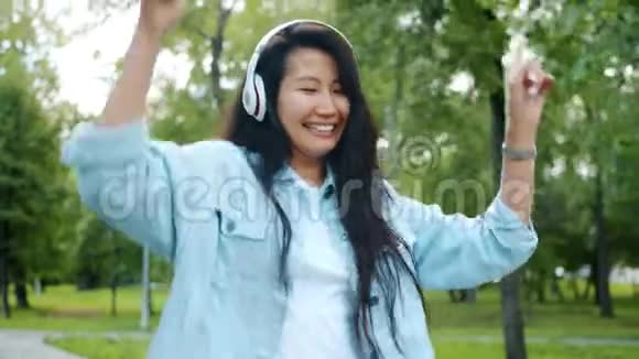 亚洲女人在户外跳舞用智能手机耳机听音乐视频的预览图
