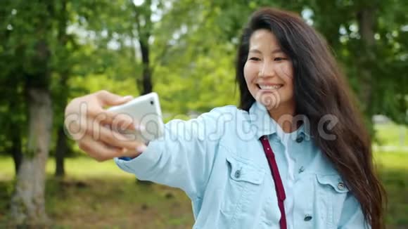 美丽的亚洲女士在公园户外自拍摆着微笑保持装置视频的预览图