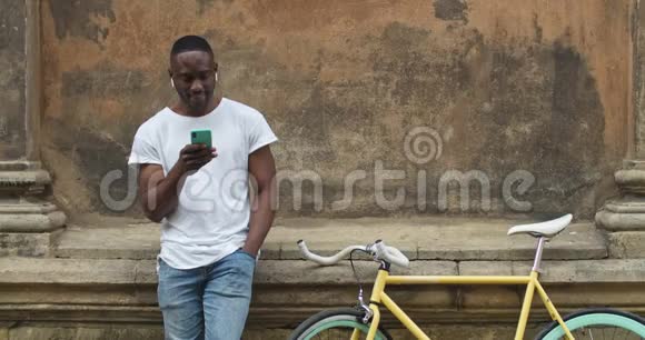 肌肉发达的非洲裔美国年轻人在耳机使用他的智能手机看屏幕和一边站着视频的预览图