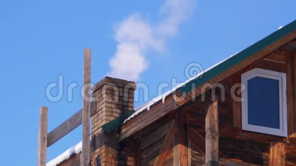 冬天在蓝天的映衬下木屋屋顶上的砖石烟囱冒出浓烟视频的预览图