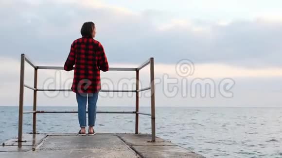 年轻迷人的快乐女人站在空浮舟上看着地平线穿牛仔裤和红衬衫的可爱孤独的女性视频的预览图