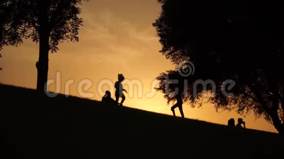 孩子们在日落时慢慢地沿着小山朝树上走视频的预览图