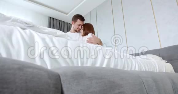 年轻夫妇在床上互相拥抱脸上带着微笑4K视频的预览图
