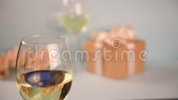 女人的手放了一杯白葡萄酒背景上的礼品盒浪漫的晚餐概念视频的预览图