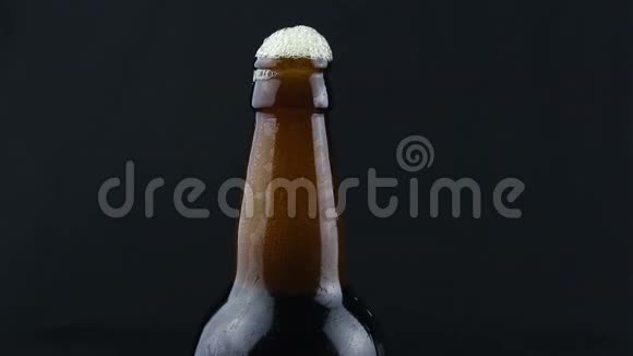 啤酒泡沫从一个雾状的瓶子里流下来泡沫顺着一瓶深色啤酒流下来深色背景下的一瓶啤酒视频的预览图