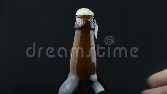啤酒泡沫从一个雾状的瓶子里流下来泡沫顺着一瓶深色啤酒流下来深色背景下的一瓶啤酒视频的预览图
