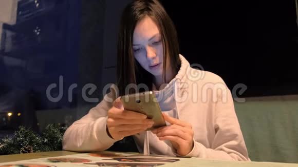 女人晚上在咖啡馆里浏览手机视频的预览图