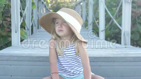 戴草帽的时髦小女孩独自坐在公园里视频的预览图