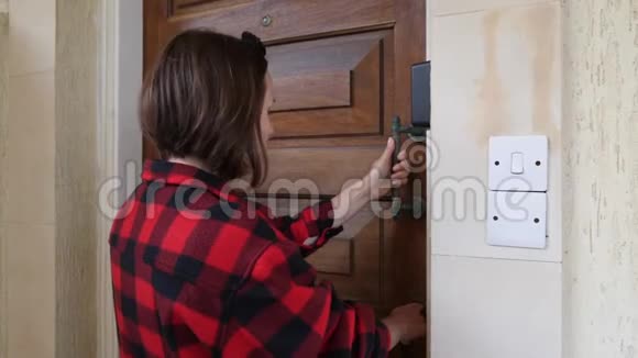 年轻的黑发白种人穿着红色格子衬衫用钥匙关上巨大的木门离开了房子视频的预览图