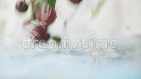 成熟的樱桃和水溅在蓝色的木桌上特写慢镜头视频的预览图