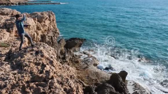 年轻人站在石头上把石头扔进水里站在悬崖边上的白人男孩把石头扔进海里曼斯坦视频的预览图