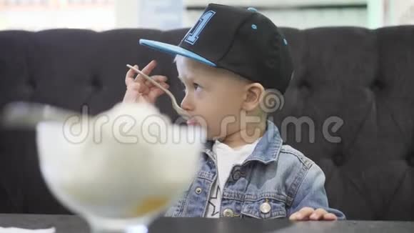 可爱快乐的小男孩在咖啡馆里吃冰淇淋小金发幼儿在自制的冰淇淋杯里吃冰淇淋视频的预览图