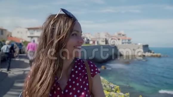 戴墨镜的年轻美女坐在明信片上模糊的背景下观看法国地中海的安蒂比斯视频的预览图