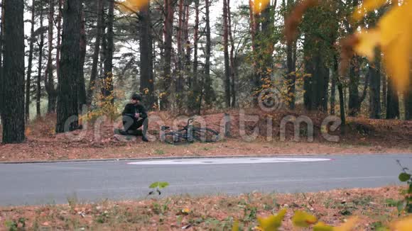 自信帅气的职业男子三项全能运动员戴着头盔和太阳镜坐在秋季公园里经过艰苦的道路训练后休息视频的预览图