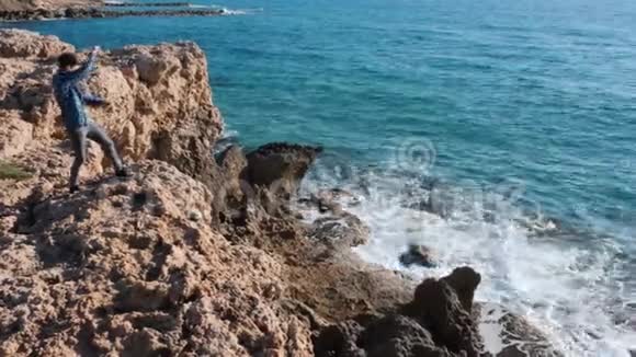 年轻人站在石头上把石头扔进水里站在悬崖边上的白人男孩把石头扔进海里曼斯坦视频的预览图