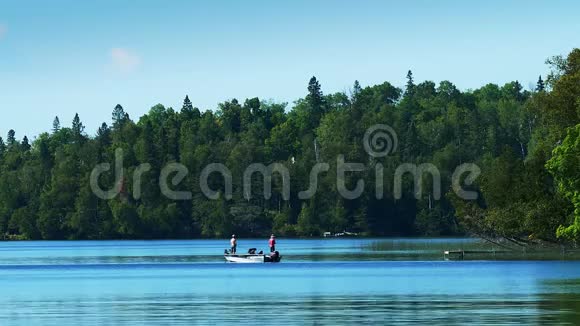 美丽的明尼苏达湖海岸线上有森林蓝天和水还有一艘渔船有两个人在捕鱼视频的预览图