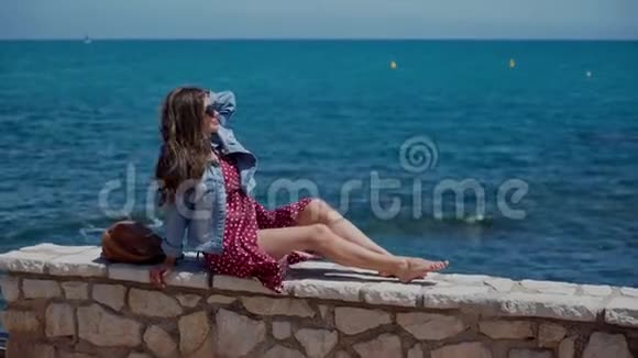 穿着红色夏装的女人坐在度假城安提布海滨的低矮石墙上头发挺直视频的预览图