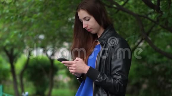 一个微笑的女孩在春天的斯洛文尼亚户外寻找她手机上的信息视频的预览图
