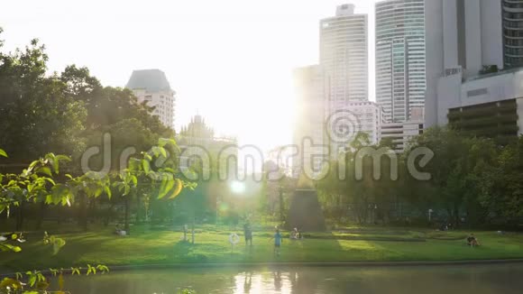 人们在公共公园放松湖和绿树与摩天大楼视频的预览图