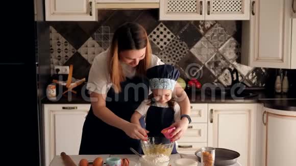 快乐的年轻妈妈带着一个小女儿在家厨房准备松饼视频的预览图
